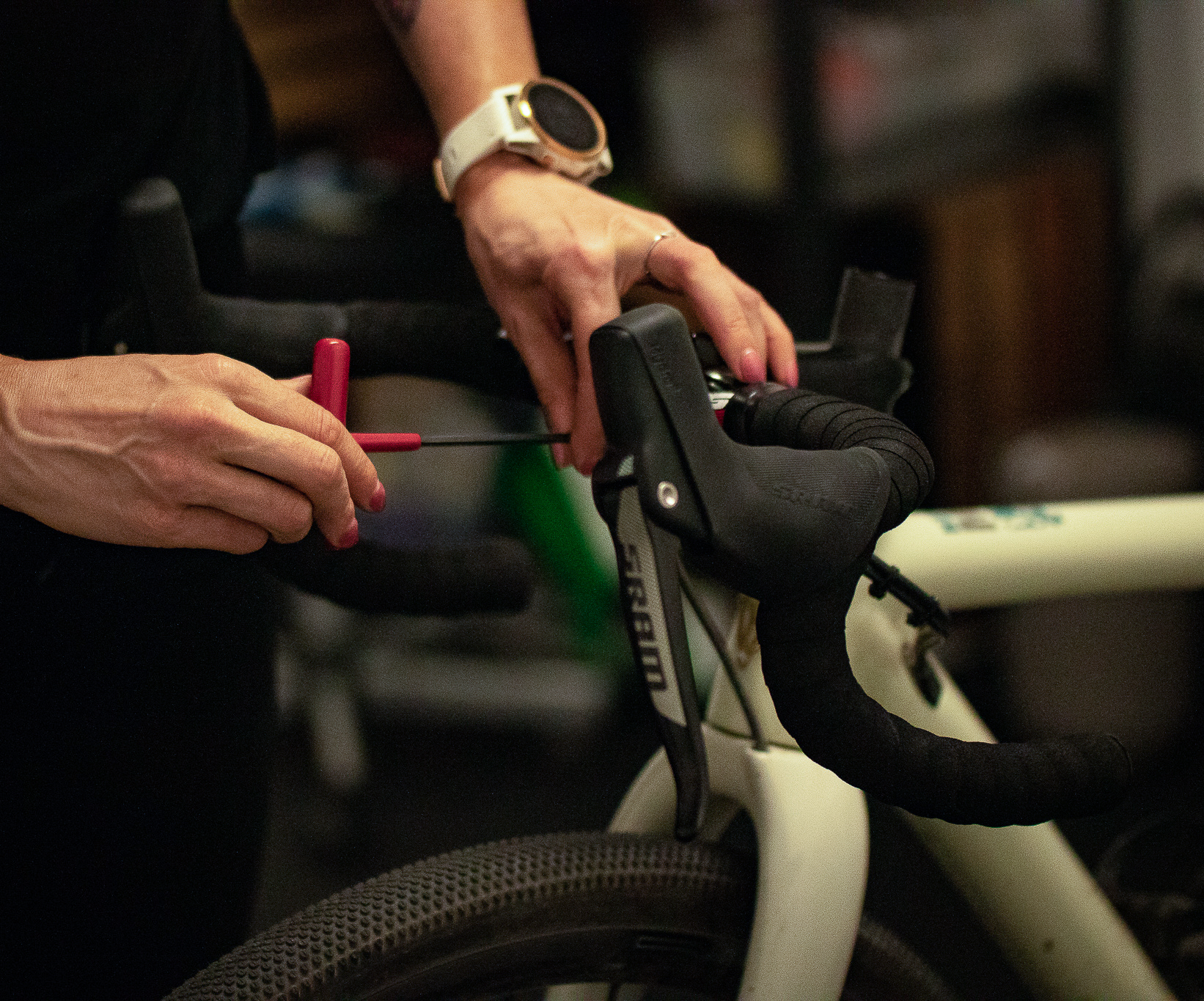 Person using a red tool to adjust the brake lever on a white road bike with black handlebars.