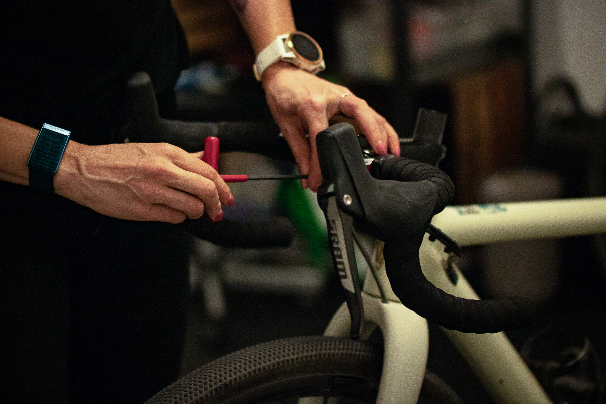 Person adjusting the brake cable on a white bicycle's black handlebar using a red tool.